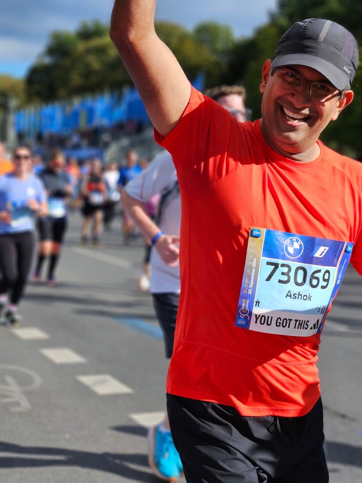 Ashok, arm raised and smiling, running the 2024 Berlin Marathon